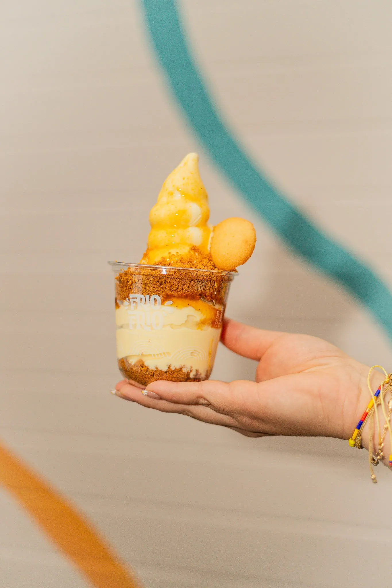 Chinola Cheesecake soft serve cup with passion fruit jam, Biscoff crumble and a cookie on top, held on an open hand