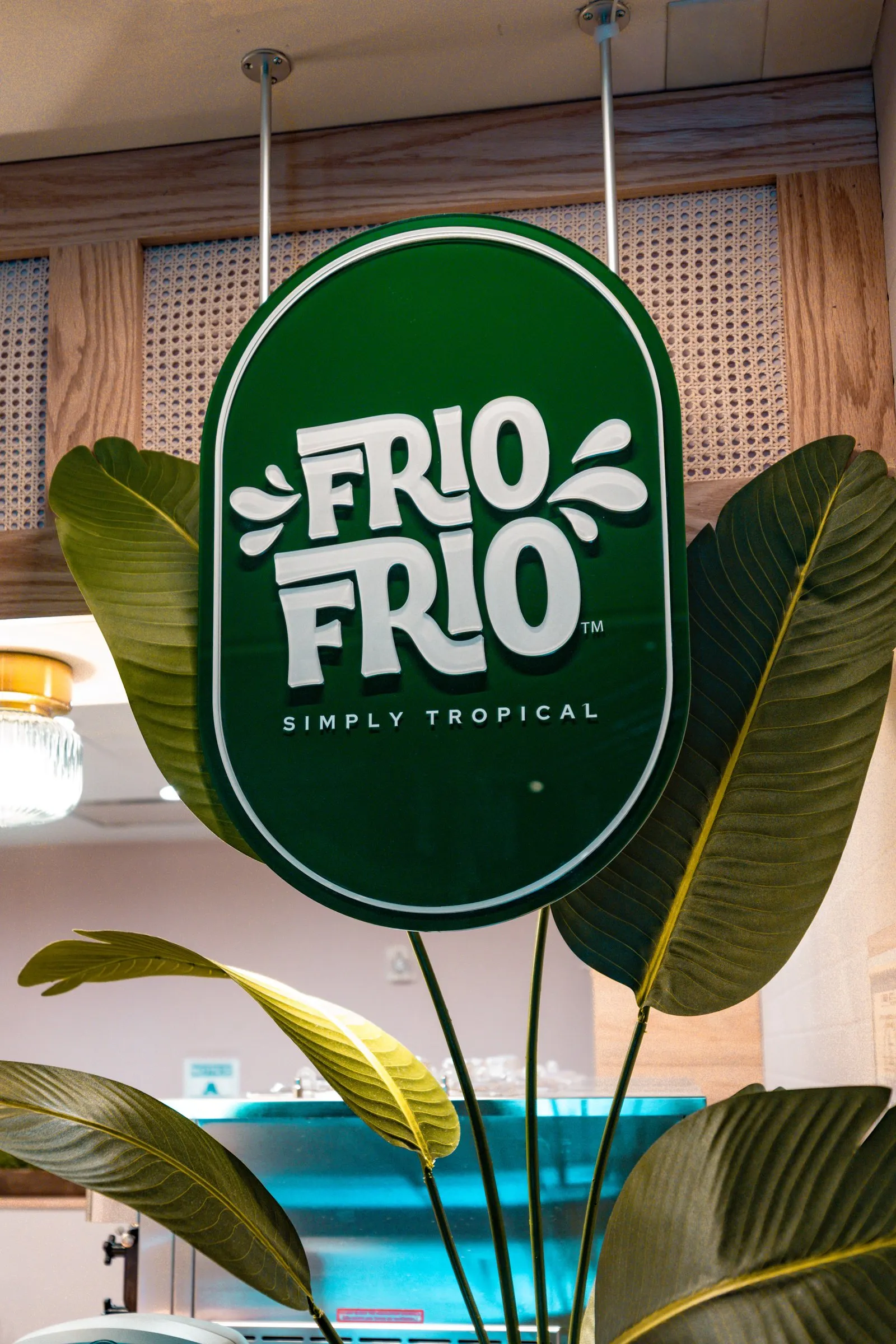 Green Frío Frío “Simply Tropical” sign hanging among tropical plants