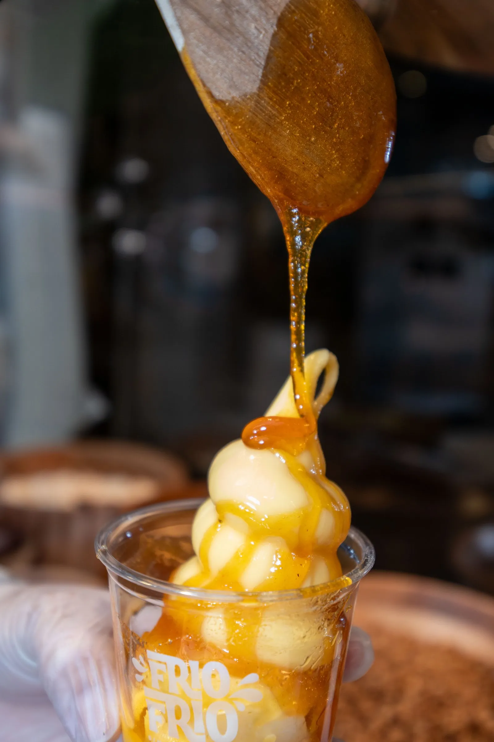 Caramel sauce being drizzled from a wooden spoon onto a soft serve cup