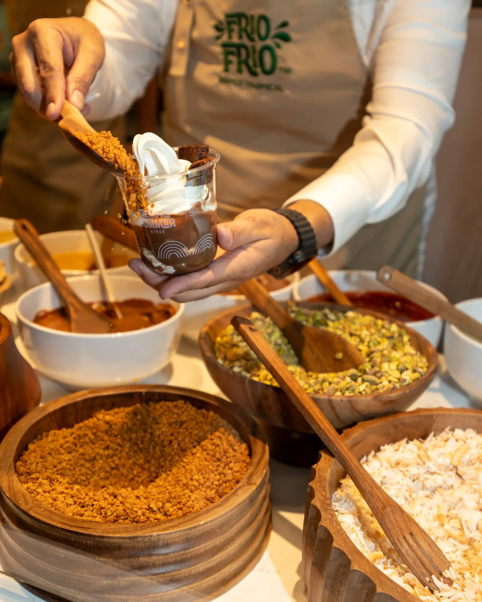 Frío Frío team member spooning cookie crumble onto a soft serve cup